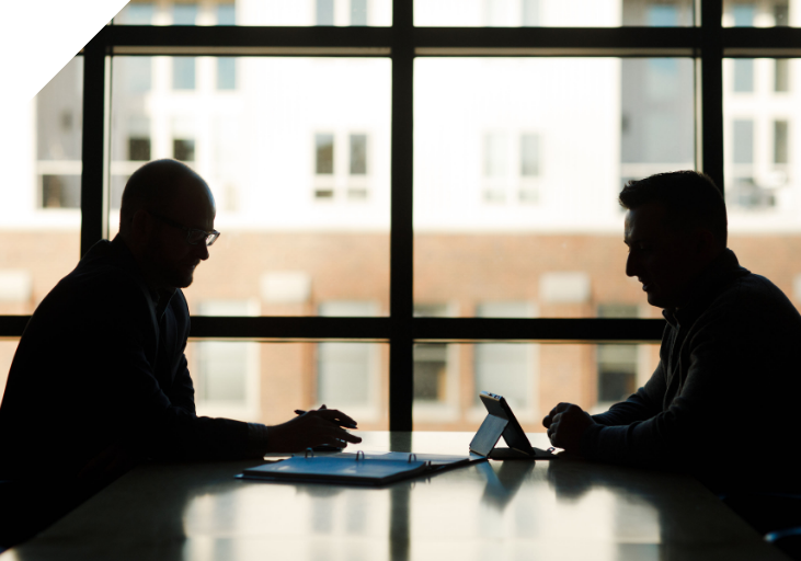 Two men sitting at a table with a tablet and binder