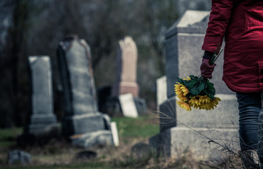 Person carrying flowers while visiting the gravesite of a loved one in a cemetery.