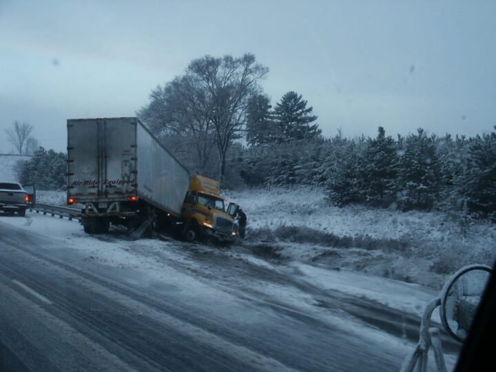 semi-truck partially off a snowy roadway and stuck in a ditch