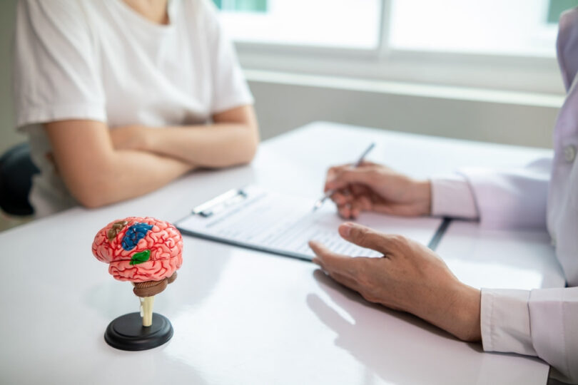neurologist consulting with a patient while holding a brain model