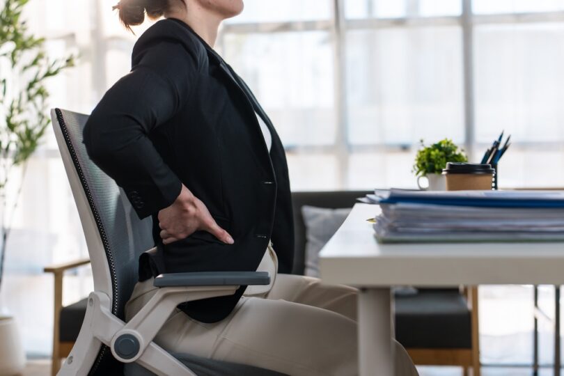 office worker holding her lower back while seated at a desk