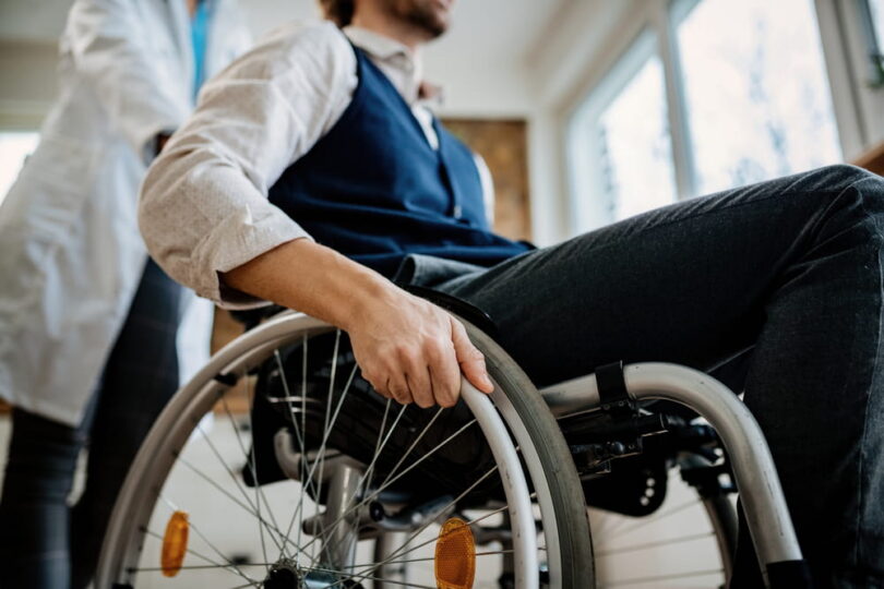 patient using a wheelchair while being assisted by a healthcare provider