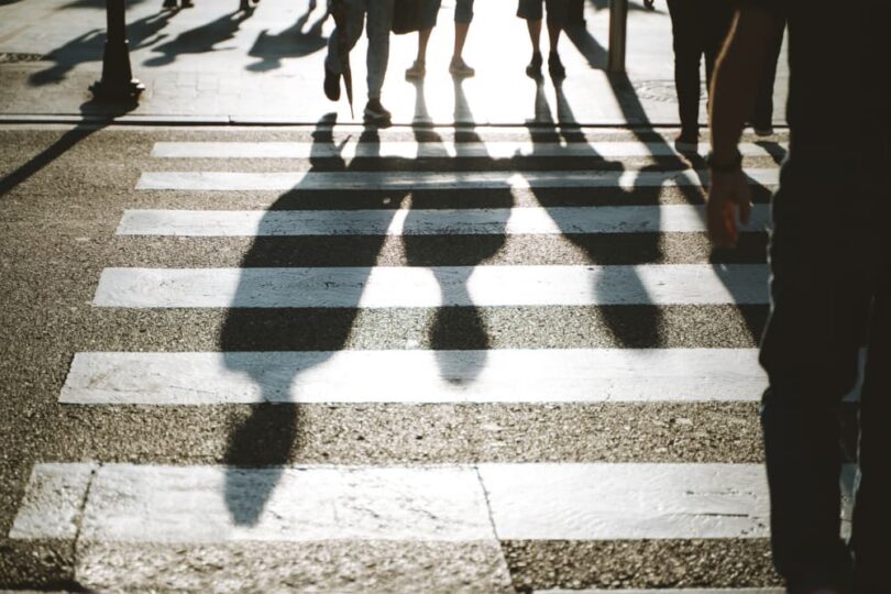 backlit silhouettes and shadows of pedestrians crossing a marked street